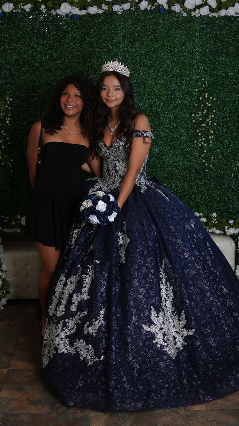 The quinceañera with a guest in front of the greenery wall